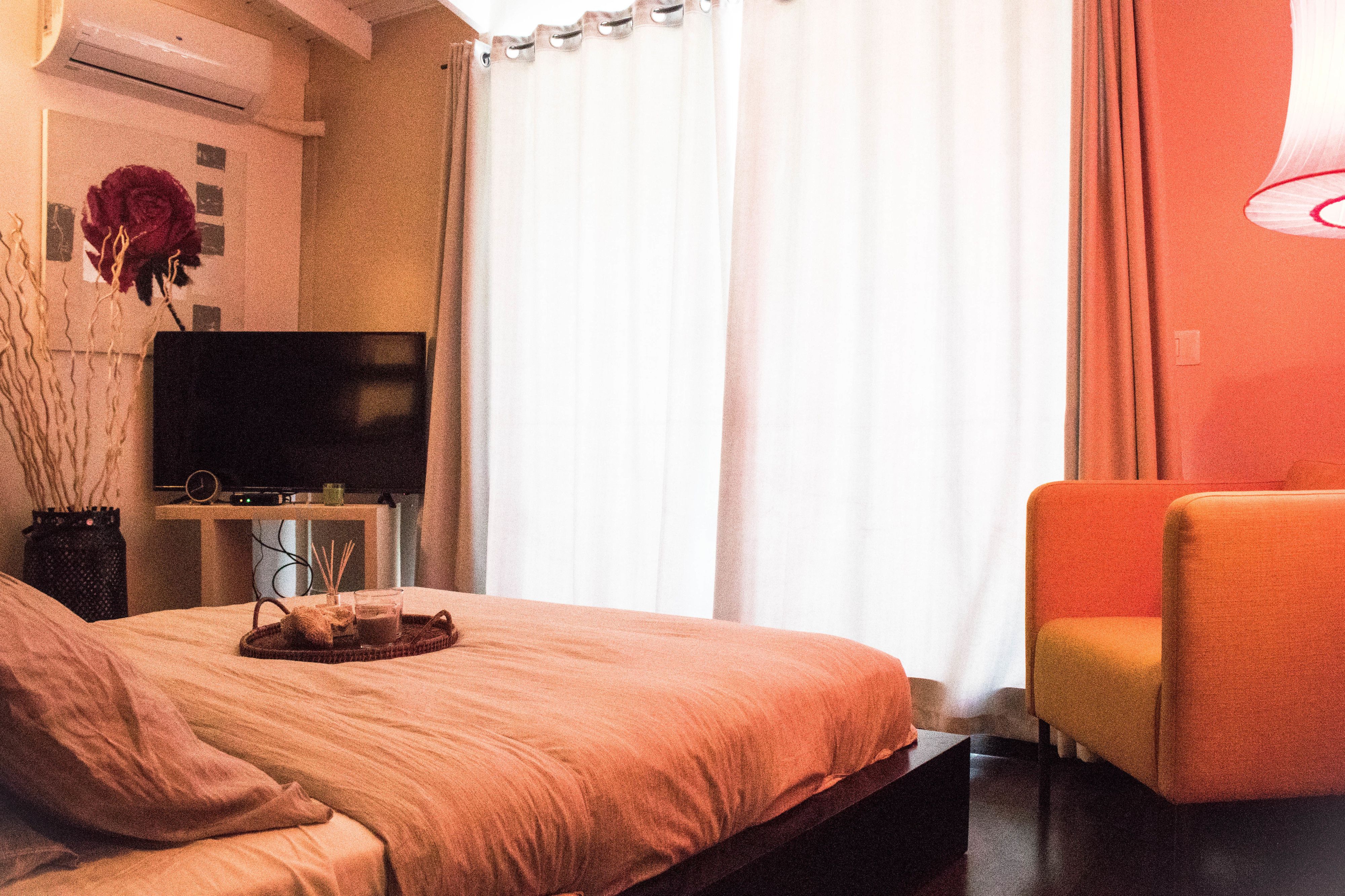 Une chambre d’hôtel avec un lit, un téléviseur posé sur un meuble, une chaise et une fenêtre avec des rideaux.