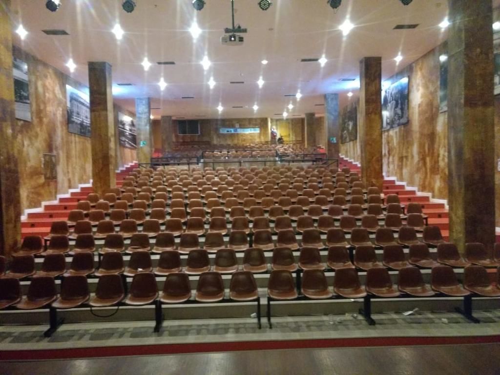 An auditorium with rows of seats, a stage at the front, and a staircase leading up to the seating area.