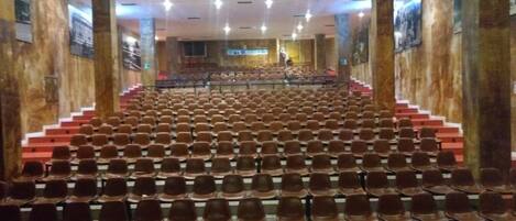 An auditorium with rows of seats, a stage at the front, and a staircase leading up to the seating area.