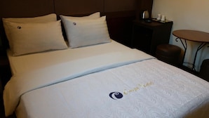 A hotel room with a bed, two pillows, a nightstand with a kettle, and a small round table with cups. - Coups (Seoul)