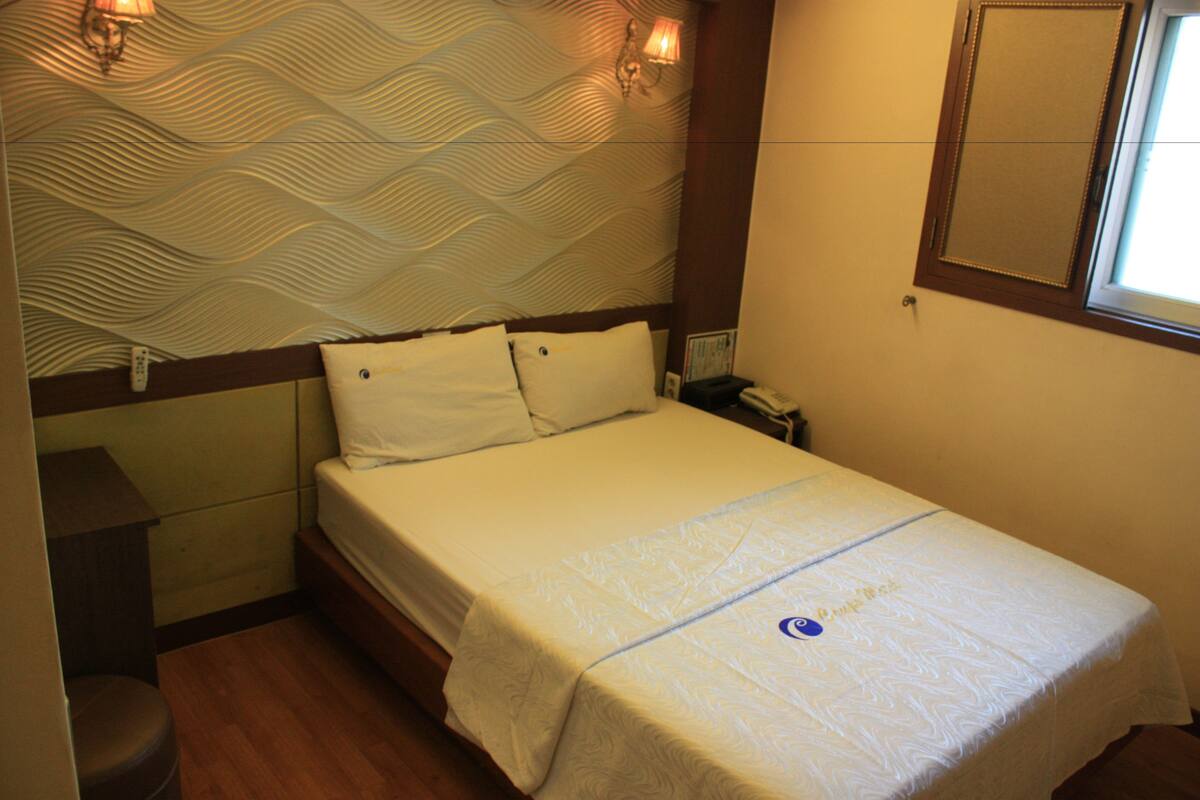 A hotel room with a bed, a nightstand, a lamp, and a window.