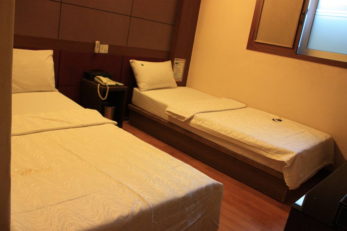 A hotel room with two single beds, a bedside table with a phone, and a small cabinet.
