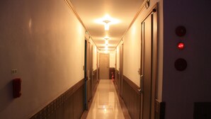 A long, narrow hallway with doors on both sides, a fire extinguisher on the left wall, and a light fixture on the ceiling. - Coups (Seoul)