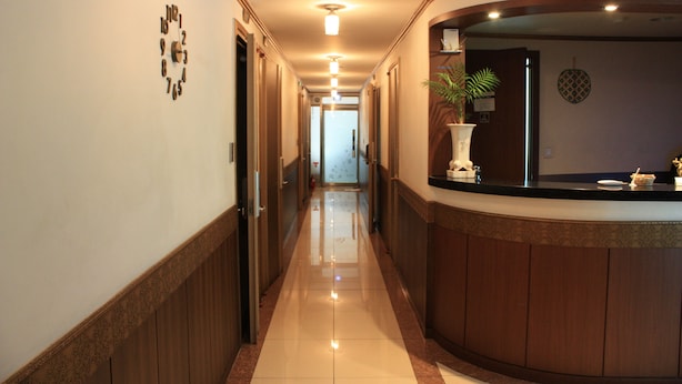 A hotel reception area with a wooden reception desk, a potted plant, and a wall clock. - Coups (Seoul)