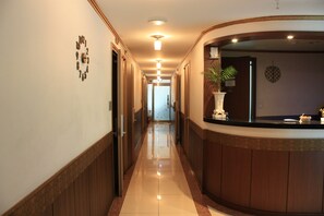 A hotel reception area with a wooden reception desk, a potted plant, and a wall clock. - Coups (Seoul)