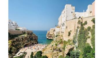 A coastal town with white buildings, a rocky beach, and a clear blue sea.