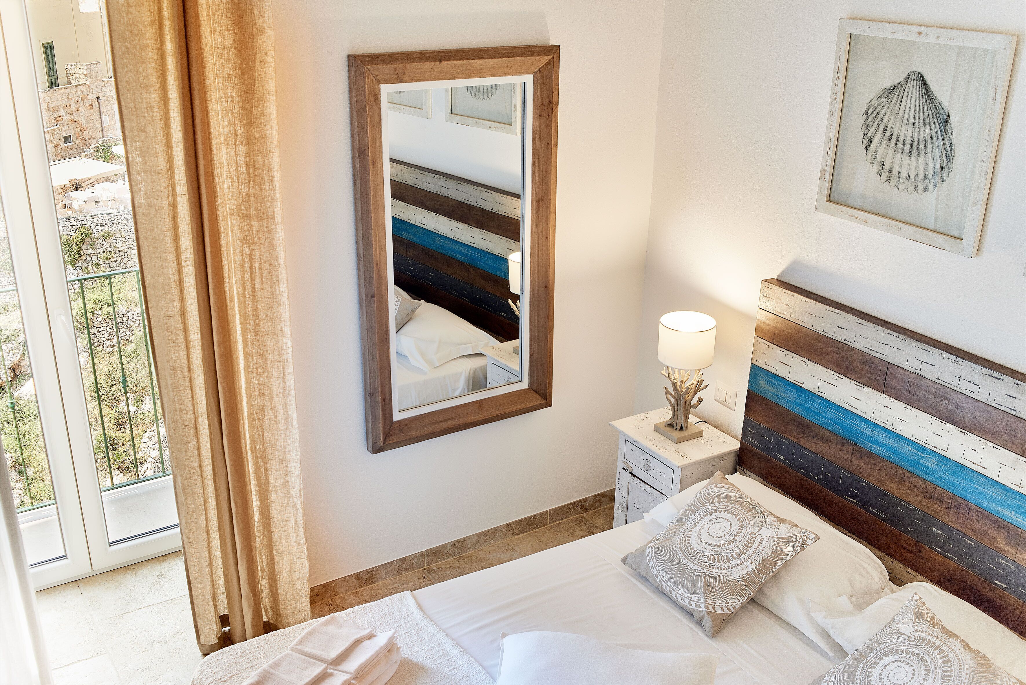 A bedroom with a bed, a nightstand, a mirror, and a view of the outdoors.