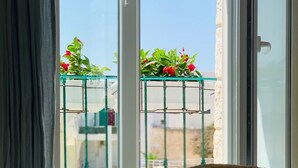 Ein Zimmer mit einem Bett, einem Fenster mit Balkonblick und einem Hut auf dem Bett.
