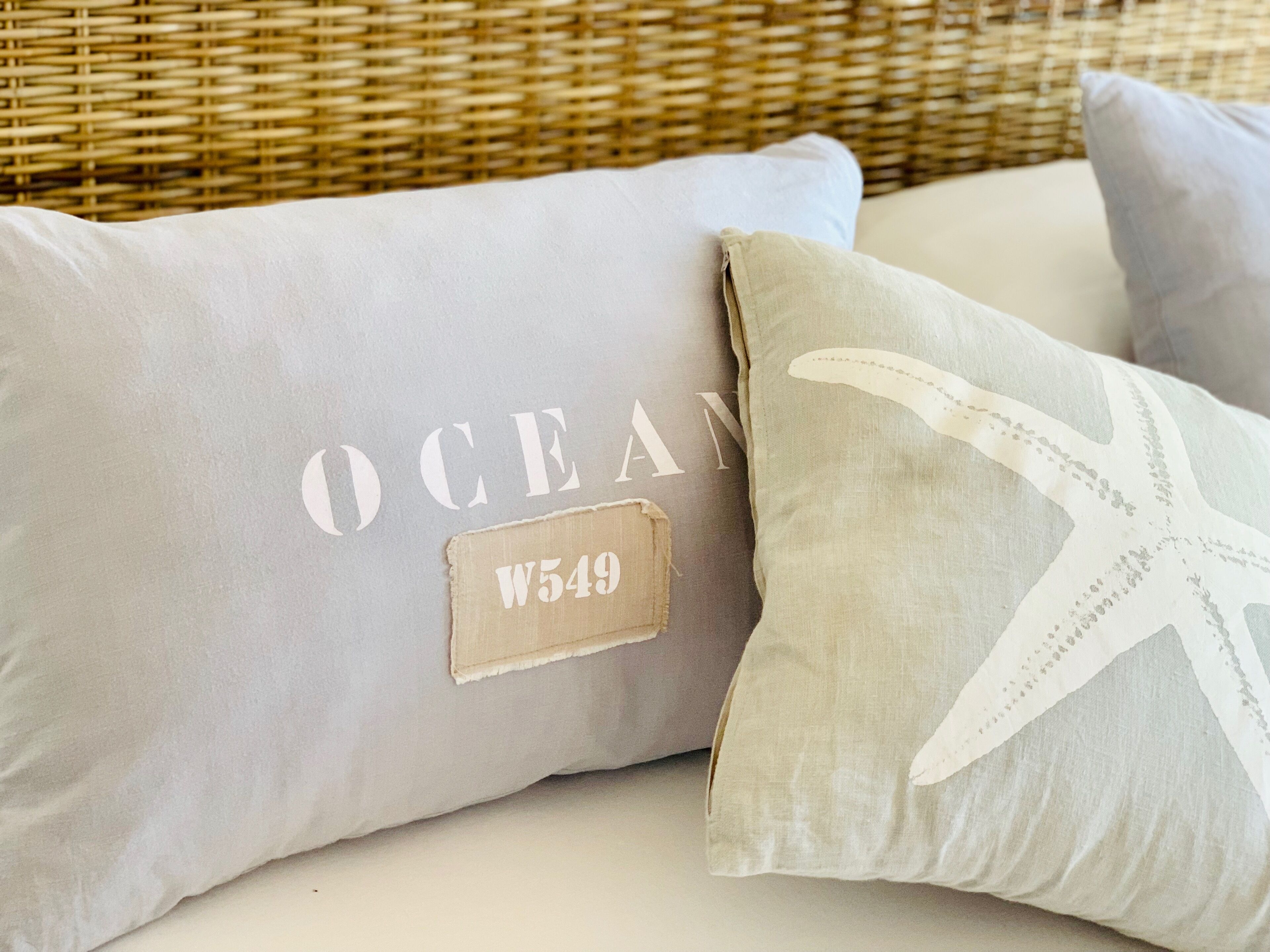 Two pillows with text and a starfish design, placed on a bed with a wicker headboard.