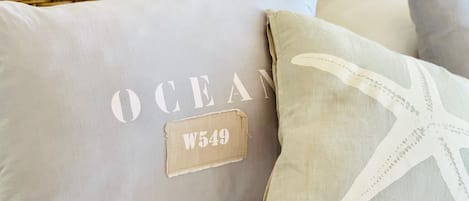 Two pillows with text and a starfish design, placed on a bed with a wicker headboard.