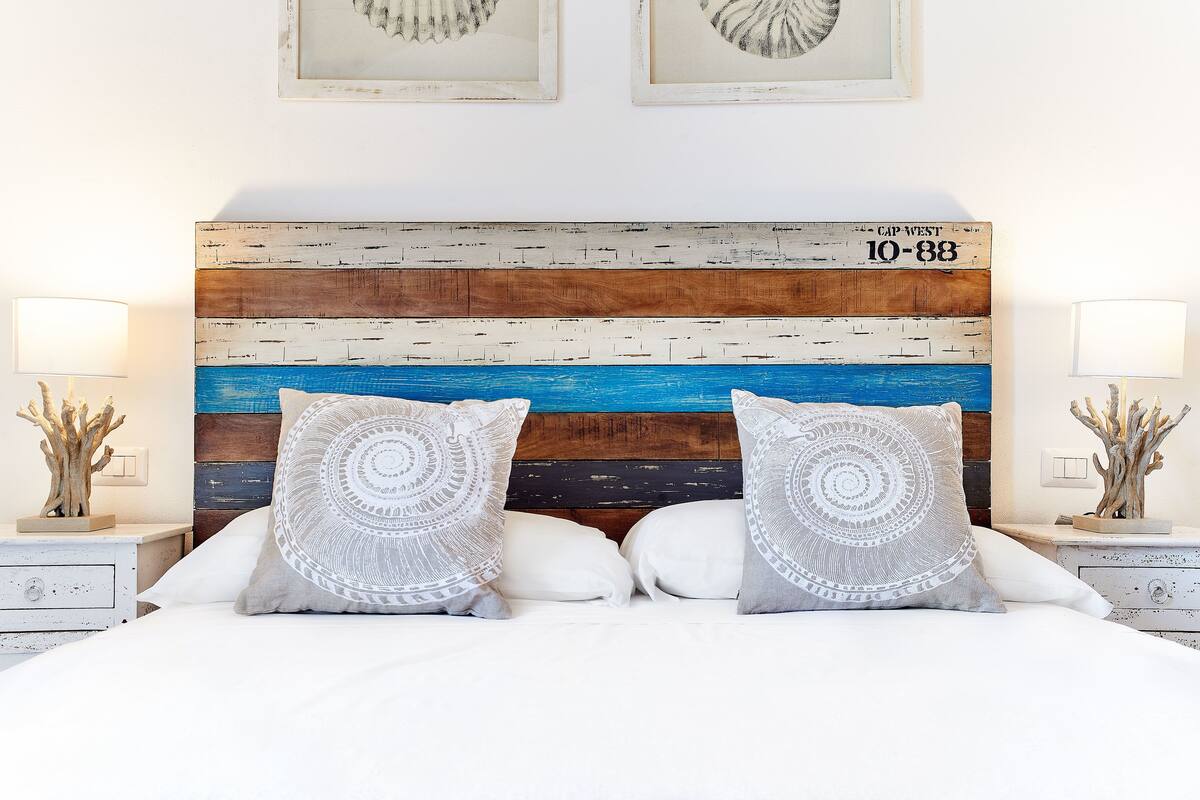 Une chambre à coucher avec une tête de lit en bois, du linge de lit blanc et des coussins décoratifs.