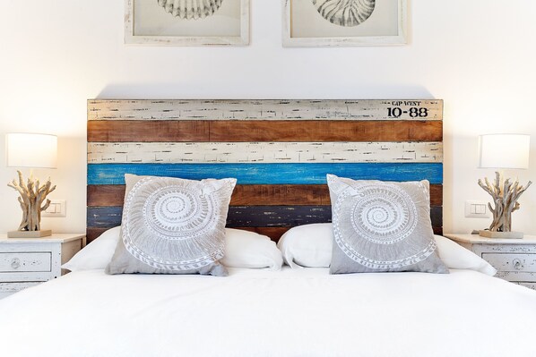 Un dormitorio con cabecera de madera, ropa de cama blanca y almohadas decorativas.