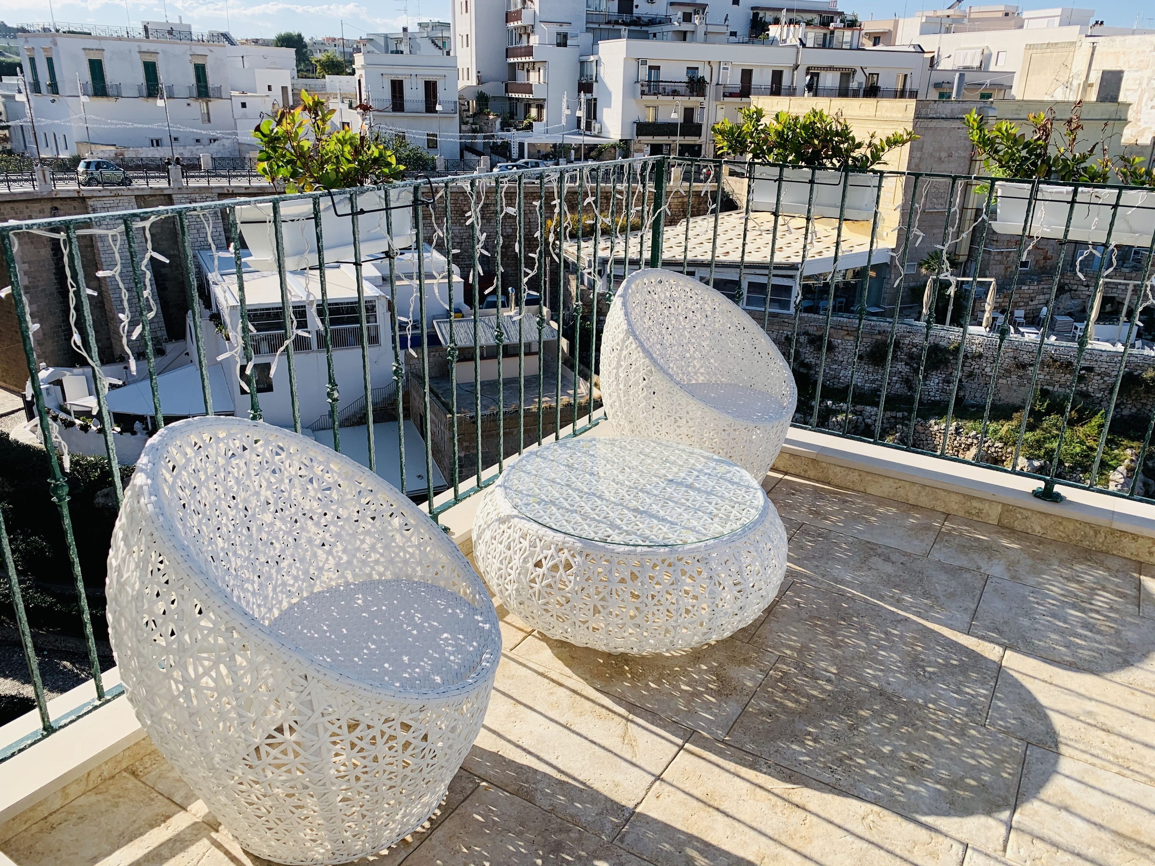Une terrasse sur le toit, avec deux chaises blanches ajourées et une table en verre, le tout entouré d’une rambarde en métal.