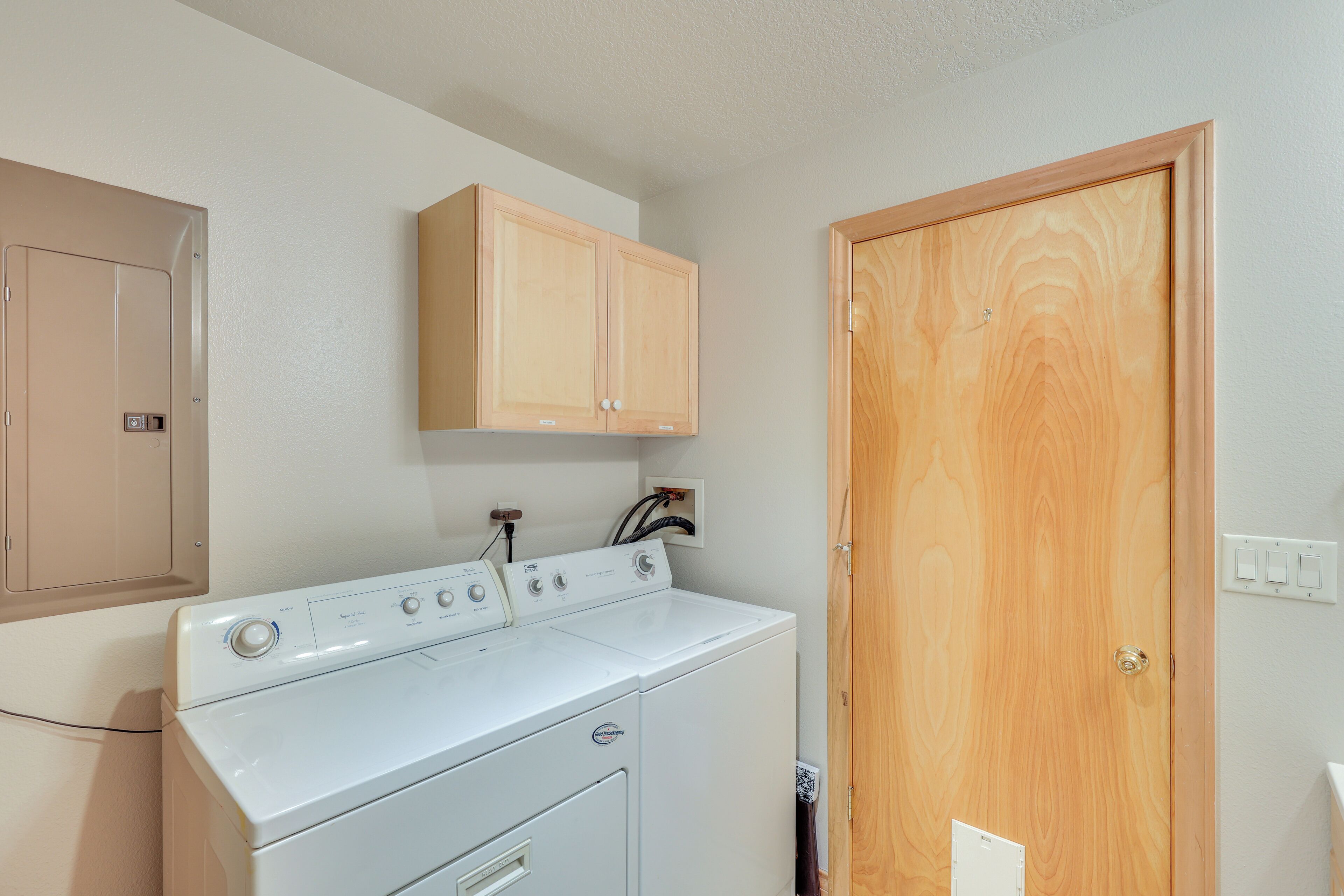 Una sala de lavandería con lavadora y secadora de carga frontal, armarios de madera arriba y una puerta de madera.