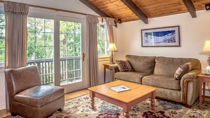 Ein gemütliches Wohnzimmer mit Holzboden, einem braunen Ledersofa, einem Holztisch und einem großen Fenster mit Vorhängen.