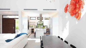 Eine moderne Küche mit einer zentralen Kochinsel, einem Essbereich mit dunklem Tisch und Stühlen sowie ein weißes Sofa mit blauen Kissen.