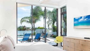 Ein Schlafzimmer mit Bett, Schreibtisch und Blick auf einen Pool und Palmen.