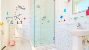 Une salle de bain moderne avec une douche à parois de verre, des murs recouverts de carreaux blancs, un lavabo blanc et des toilettes.