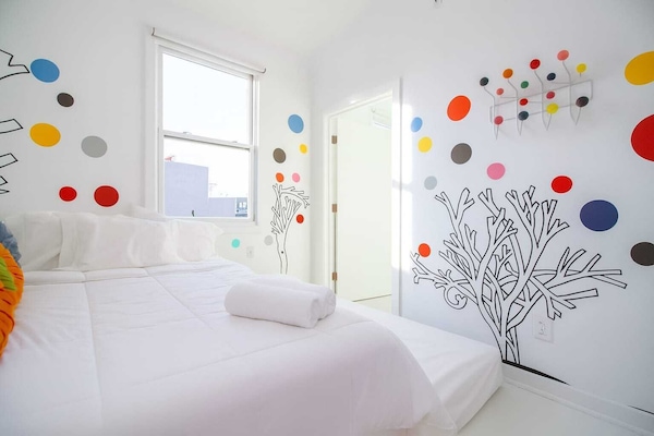 Bright, whimsical bedroom with colorful wall art, cozy bed, and natural light—clean, cheerful, and creatively designed.