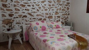 Un dormitorio con pared de piedra, cama con ropa de cama floral, mesita de noche con lámpara y radiador.