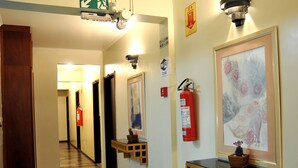 A hotel hallway with wooden benches, a fire extinguisher, and framed artwork on the walls. - Hotel Cidade (Passos)
