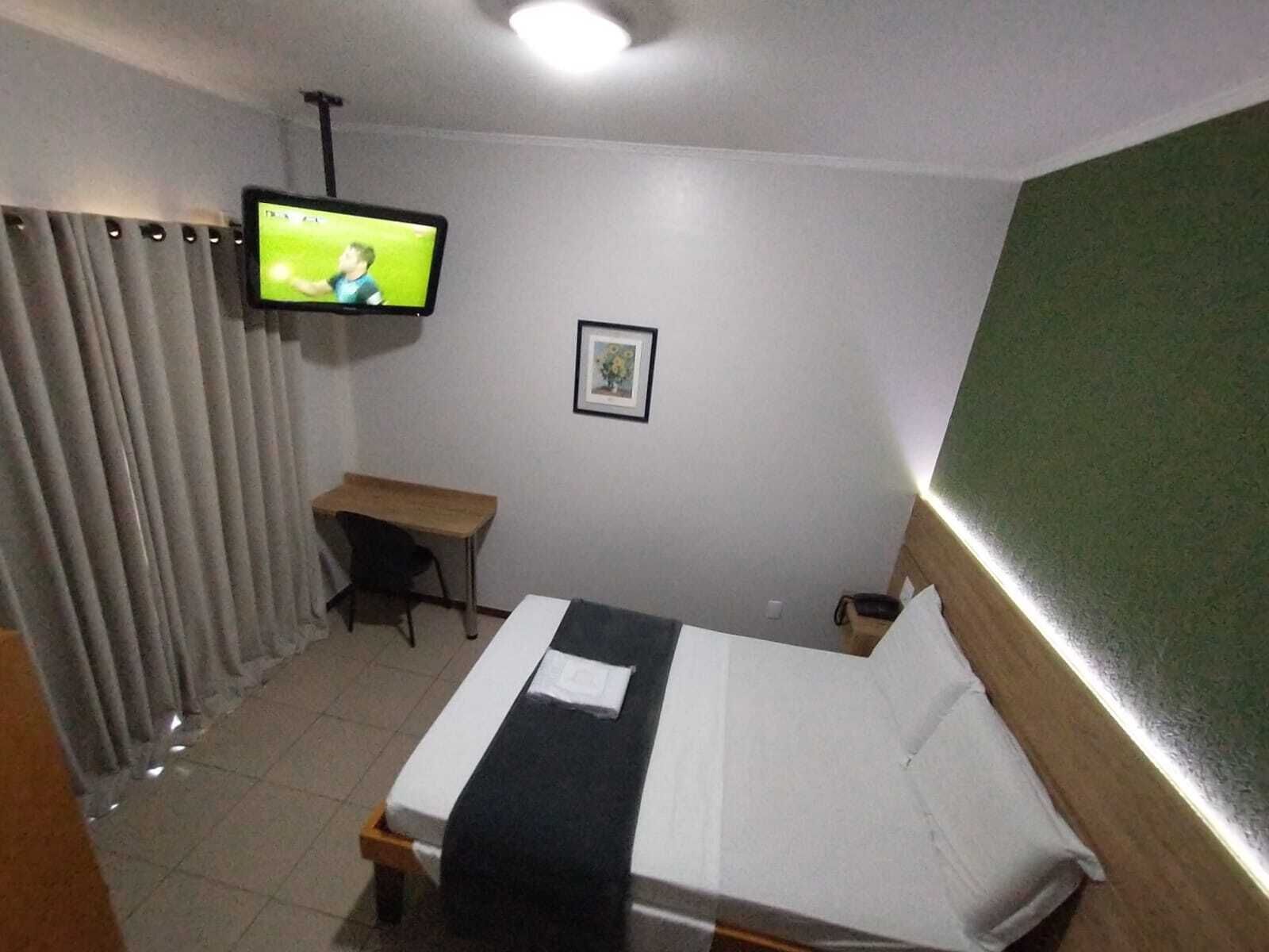 A hotel room with a bed, a desk, a television mounted on the wall, and a framed picture on the wall.