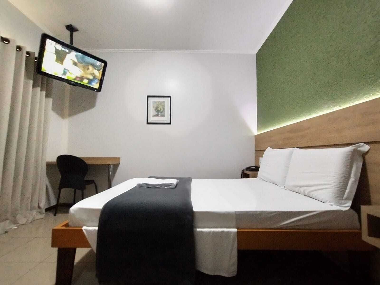 Una camera d'albergo con un letto, una scrivania, una sedia, una televisione e un quadro appeso al muro.