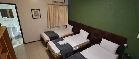 Una habitación de hotel con dos camas individuales, baño con lavamanos e inodoro, y una pared verde.