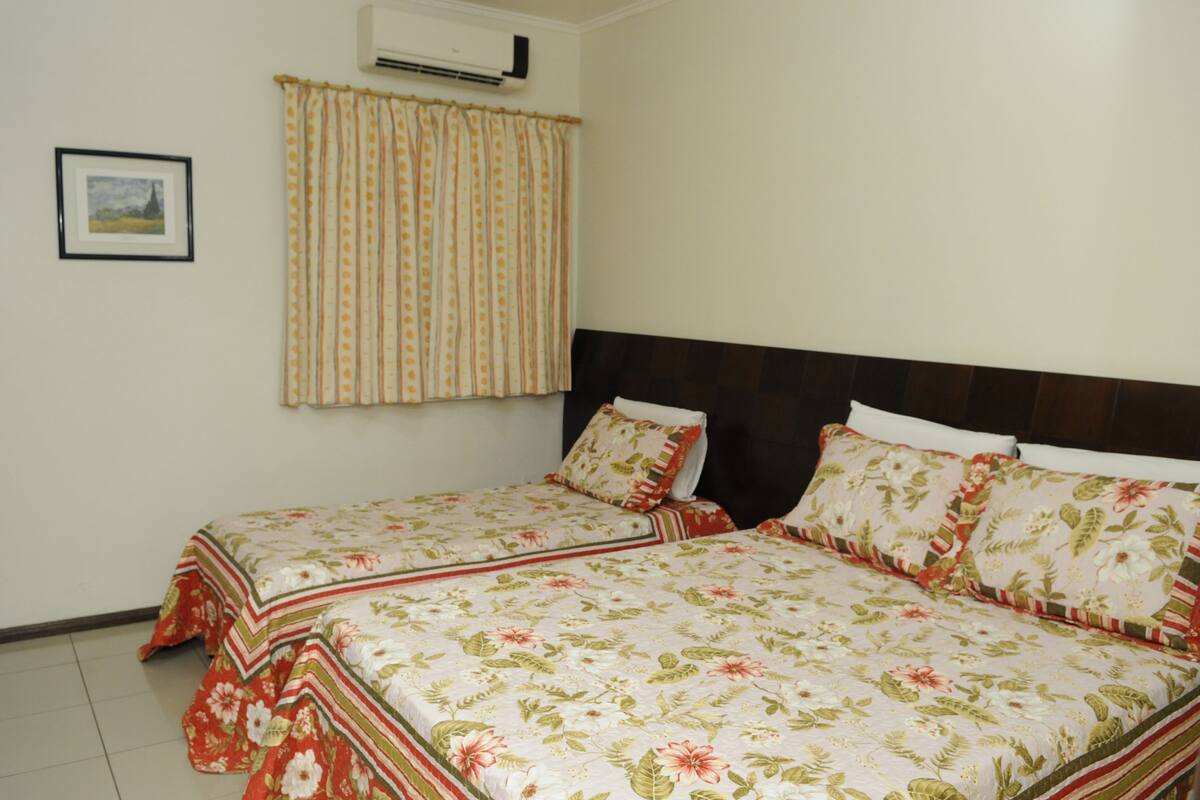 A double bed with floral bedding, a dark headboard, and a window with striped curtains.