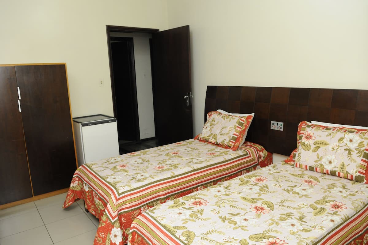A bedroom with two beds, a wardrobe, and a small table.