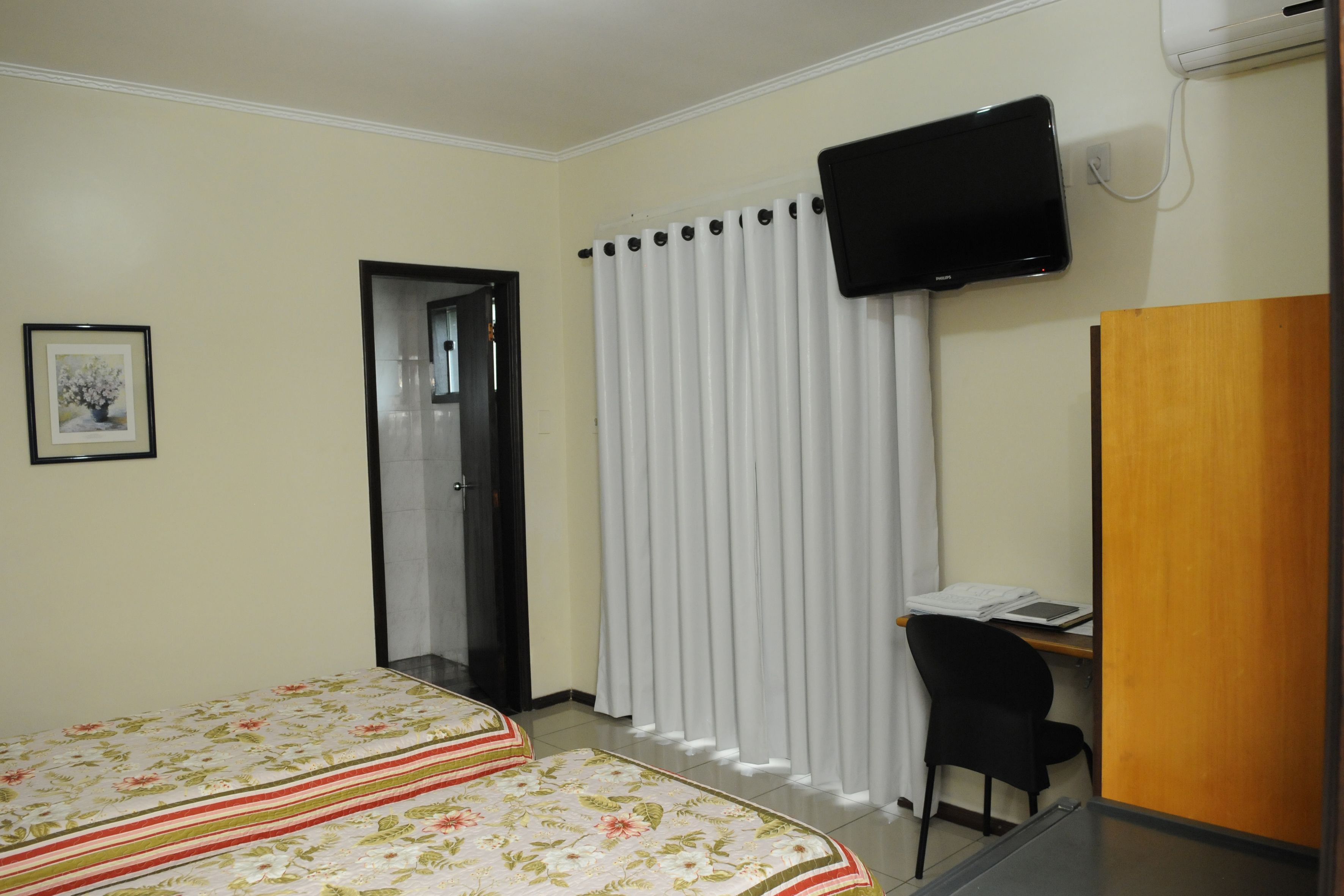 A hotel room with a bed, a desk, a chair, a television, and a door.