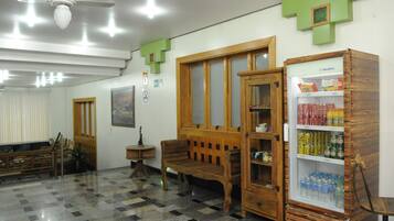 Um hall com piso xadrez, mobiliário de madeira, geladeira abastecida com bebidas e um ventilador de teto.