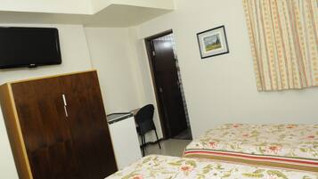 A bedroom with a bed, a desk, a chair, a wardrobe, a television, and a door leading to another room.