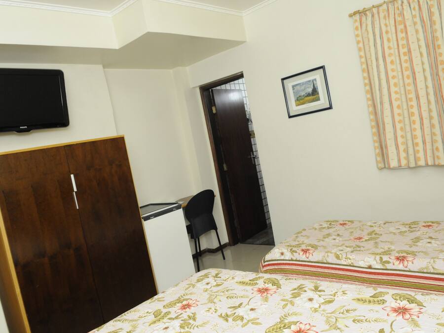 A bedroom with a bed, a desk, a chair, a wardrobe, a television, and a door leading to another room.