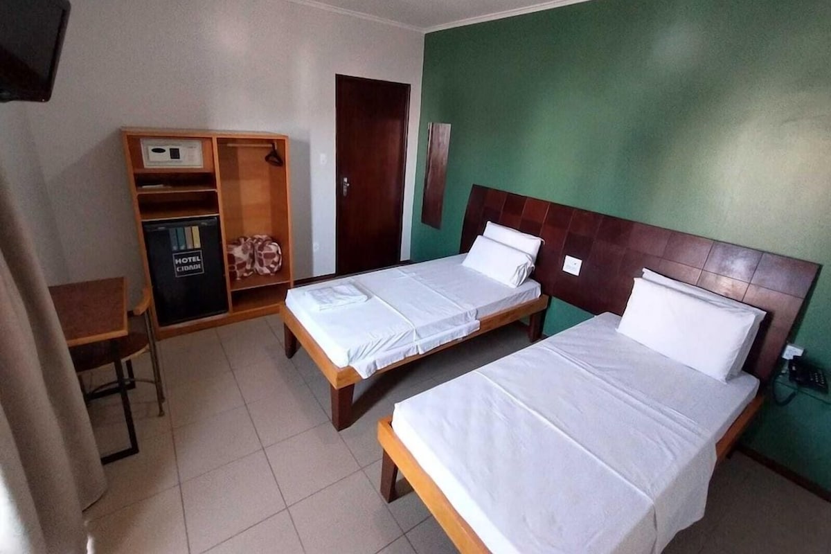A hotel room with two single beds, a wooden wardrobe, and a desk with a chair.