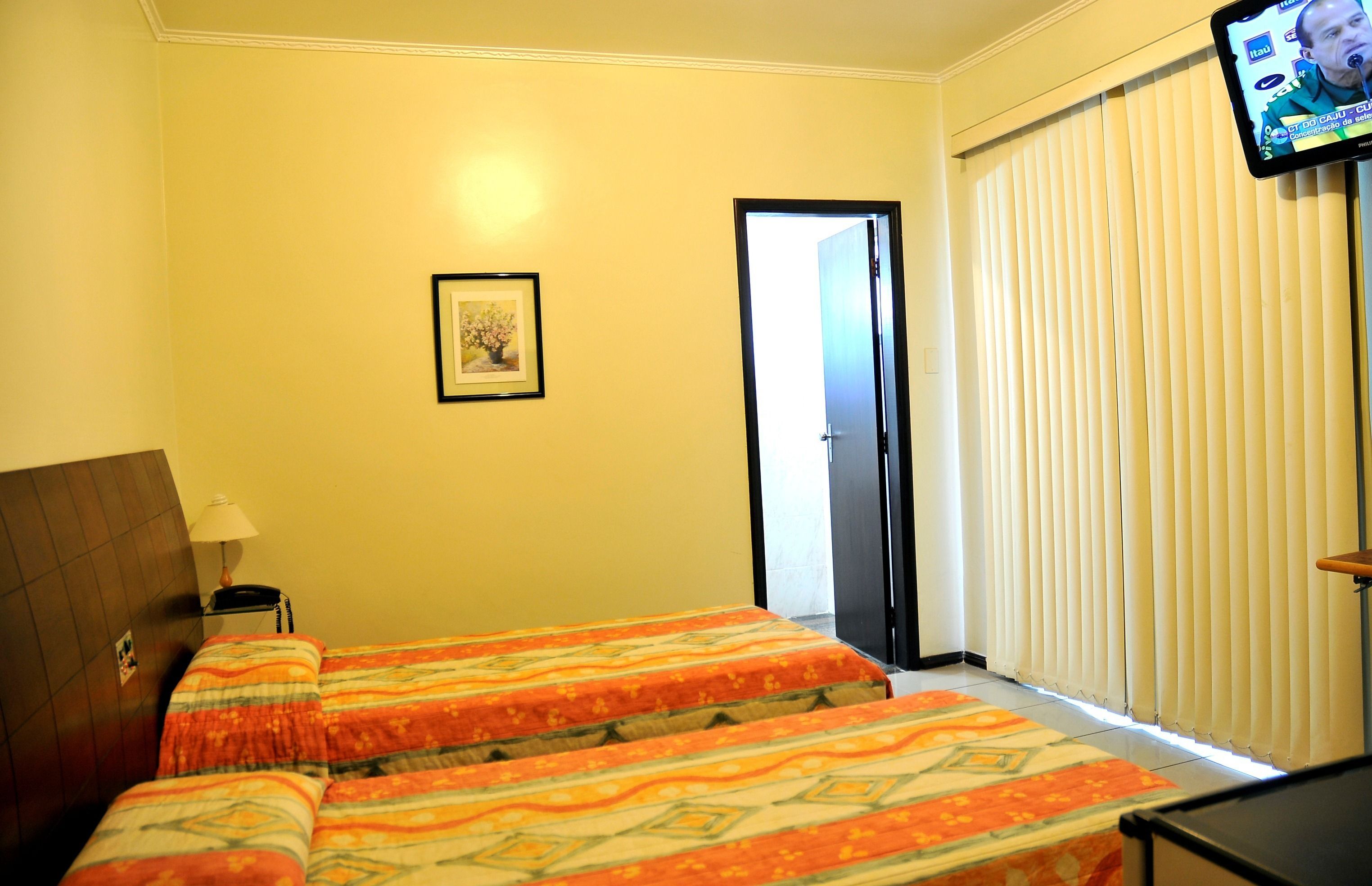 A hotel room with two beds, a framed picture on the wall, a television mounted on the wall, and a door leading to a balcony.