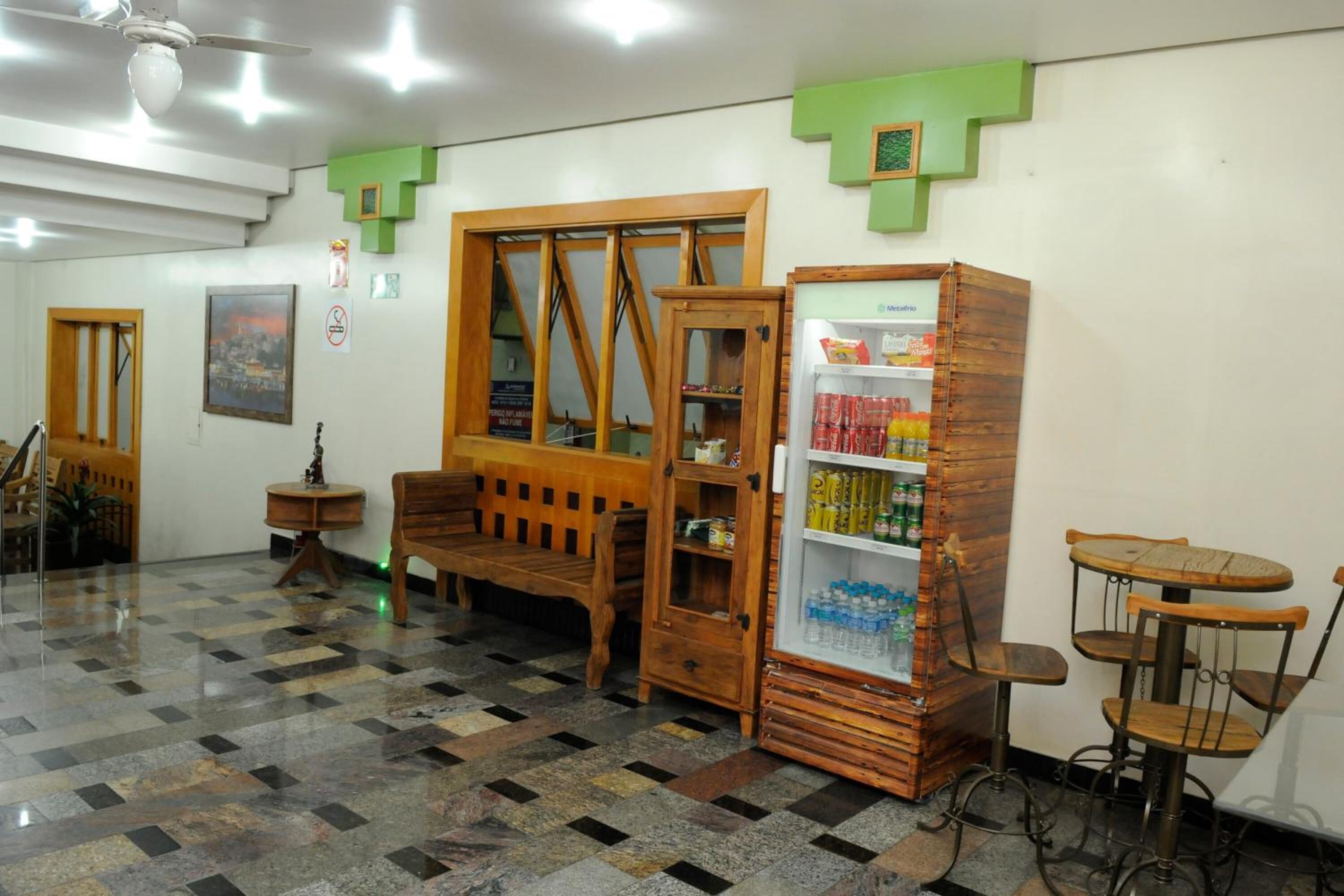 Quarto com piso xadrez, móveis de madeira, geladeira repleta de bebidas e um adorno verde na parede.