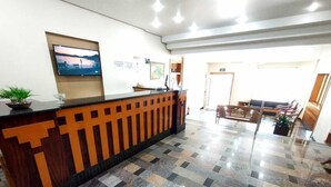 A reception area with a check-in counter, a television mounted on the wall, and a patterned floor. - Hotel Cidade (Passos)