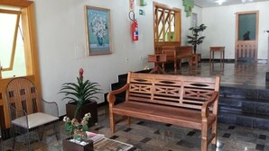 A lobby with a wooden bench, a glass table with magazines, a potted plant, and a fire extinguisher on the wall. - Hotel Cidade (Passos)