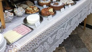 A buffet setup with various food items and a decorative tablecloth. - Hotel Cidade (Passos)