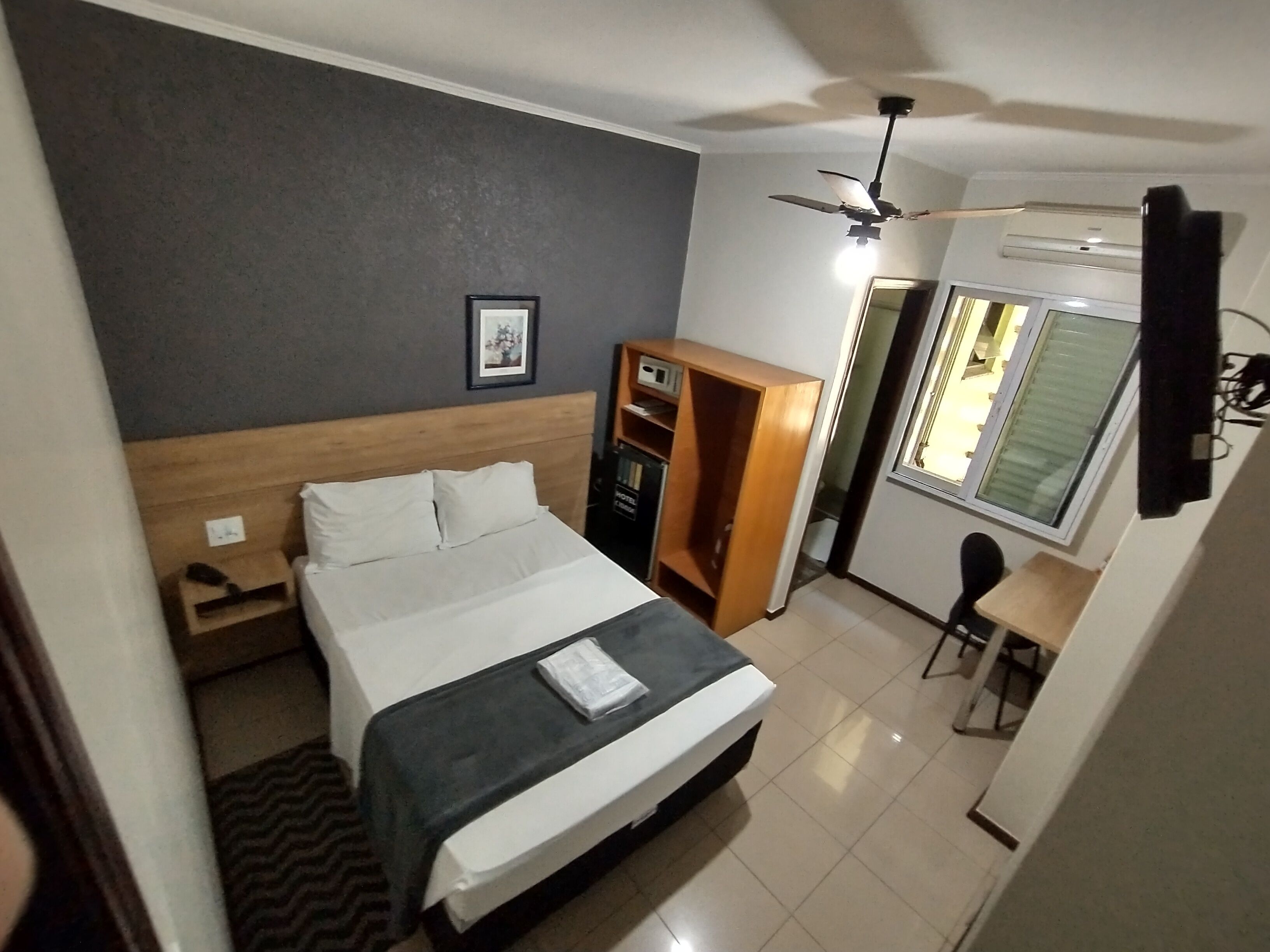 A hotel room with a bed, a wardrobe, a desk, and a ceiling fan.