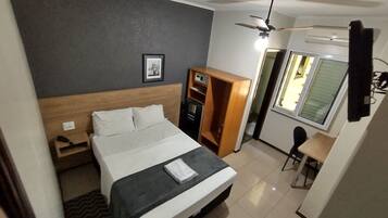 A hotel room with a bed, a wardrobe, a desk, and a ceiling fan.