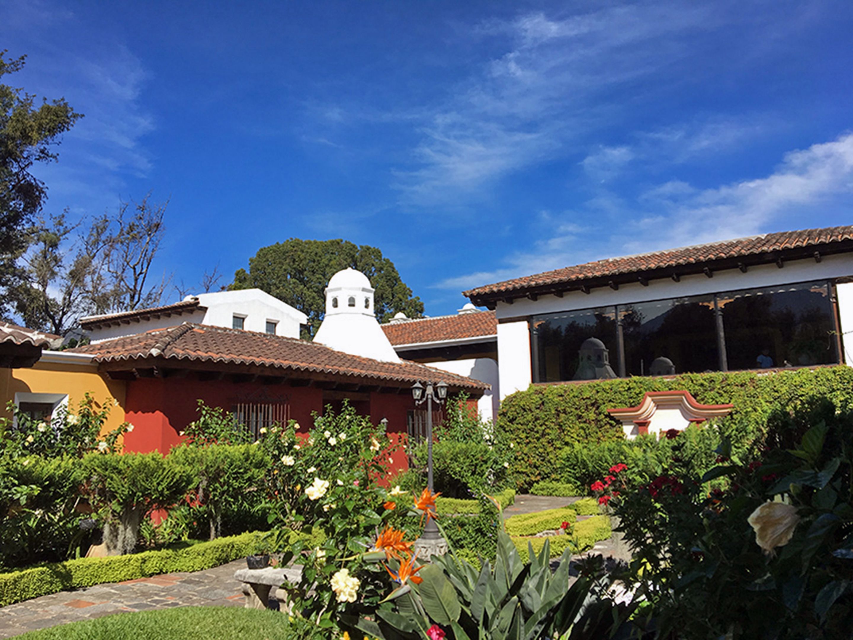 A traditional building with a white dome and red-tiled roof, surrounded by well-maintained gardens and a clear blue sky.