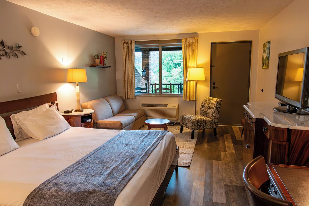 A hotel room with a bed, a sofa, a chair, a TV, and a window with curtains.