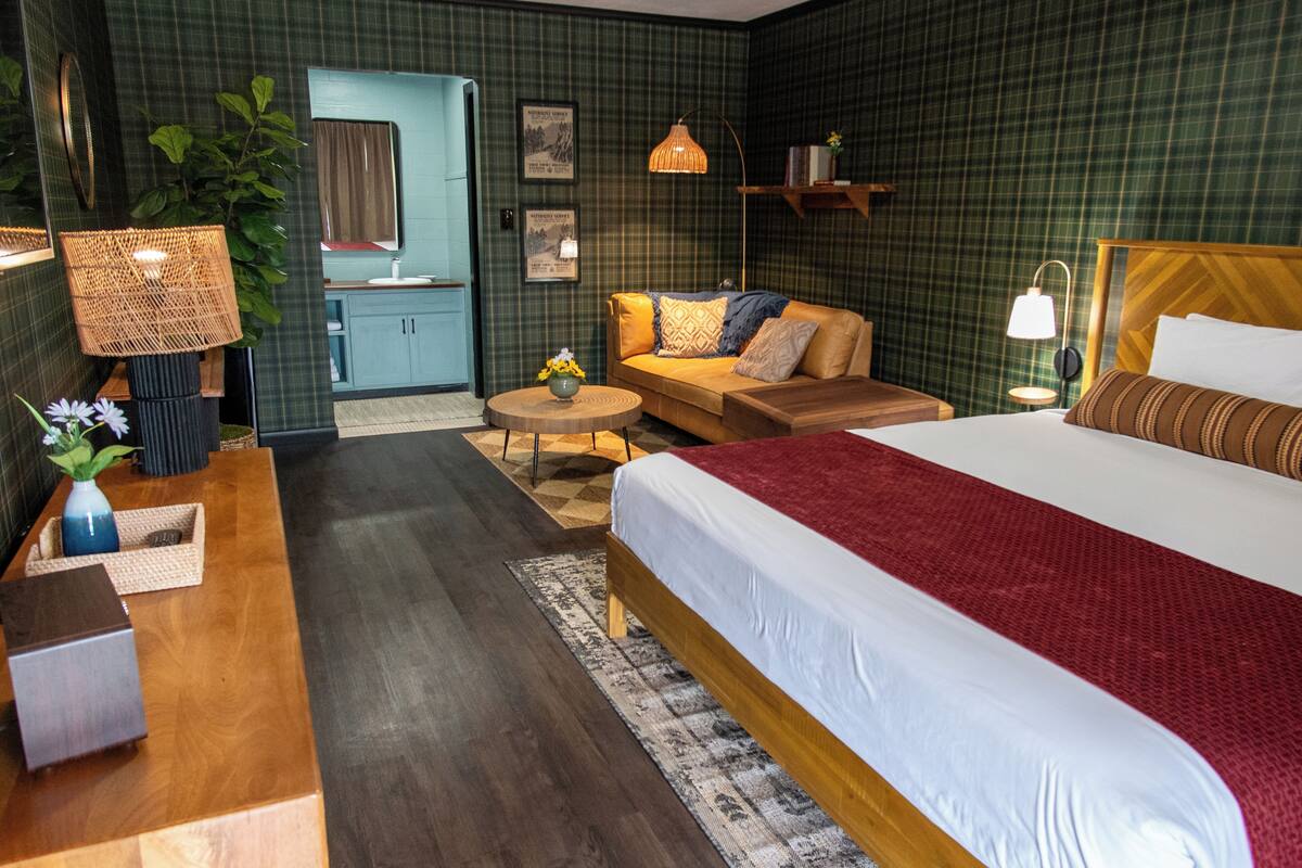 A hotel room with a large bed, a sofa, a small table, a lamp, and a mirror.