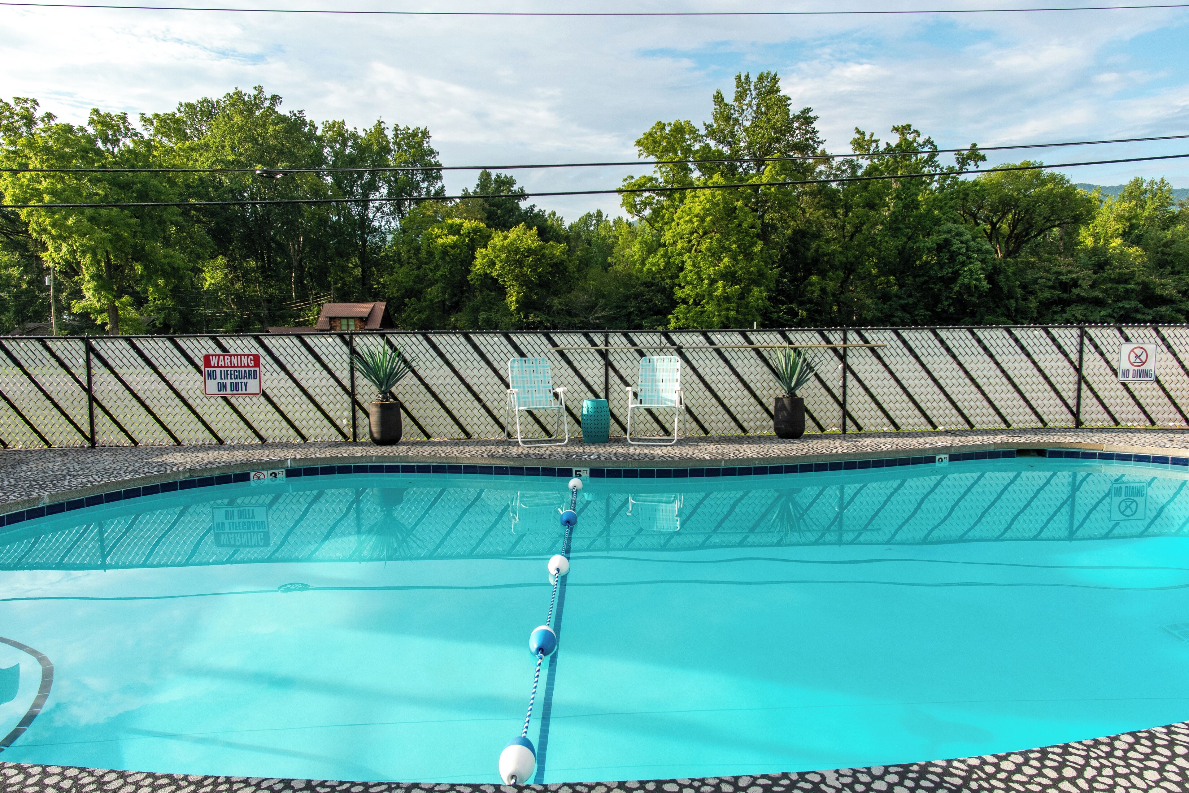 A swimming pool with a safety warning sign, a fence, and potted plants.
