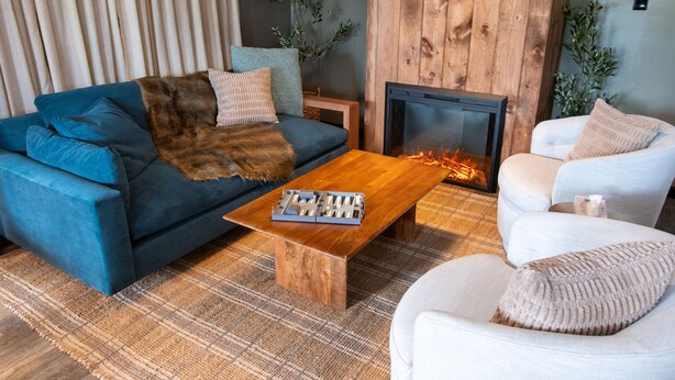 A living room with a blue sofa, a white armchair, a wooden coffee table, and a fireplace.
