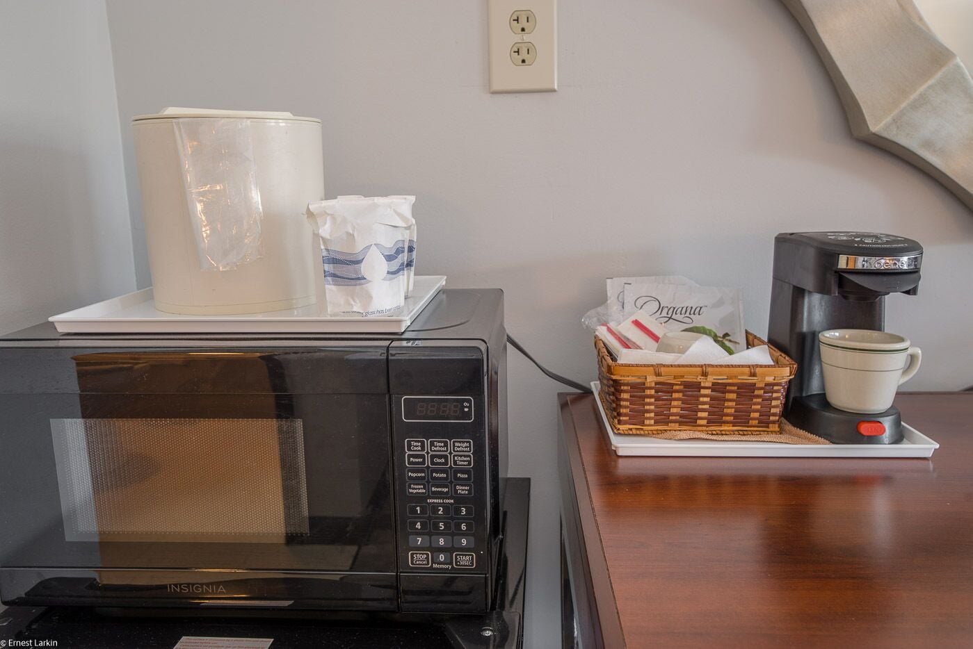 Un four à micro-ondes est posé sur une table, à côté d’un panier contenant une cafetière, une tasse et une boîte de mouchoirs.