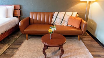 Una habitación con un sofá de cuero marrón, una cama de madera, una mesita de madera con un jarrón de flores y una lámpara.