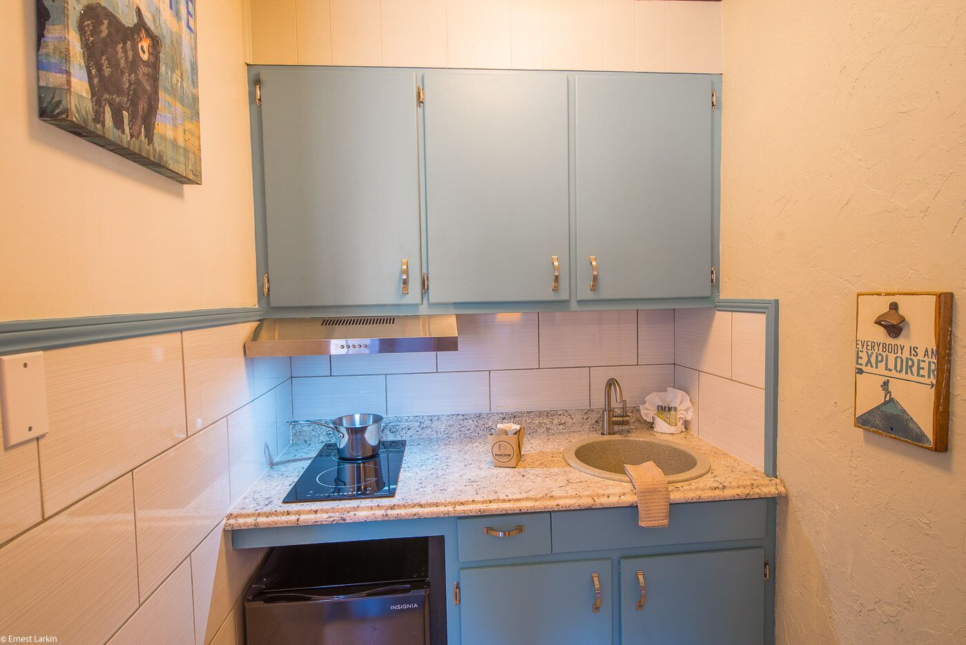 A compact kitchen with light blue cabinets, a stainless steel range hood, a built-in dishwasher, and a granite countertop.